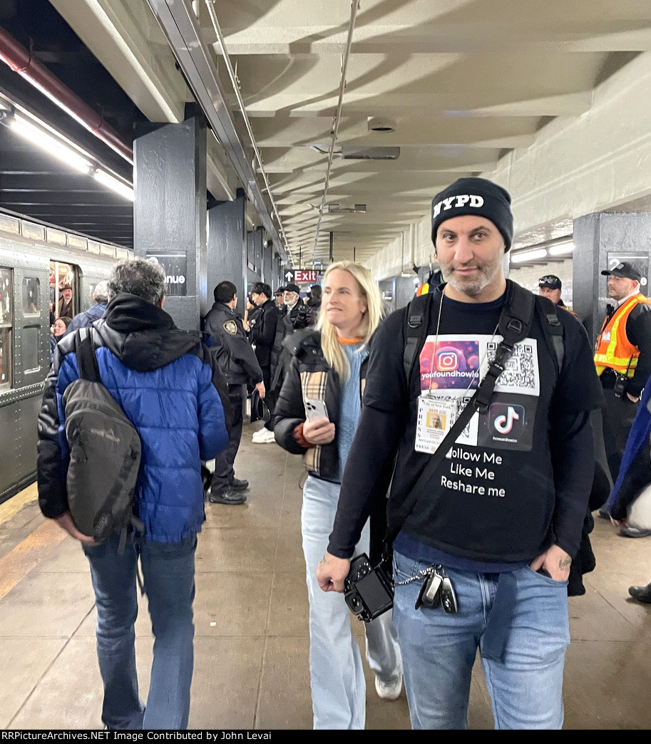 A man wearing a social media themed shirt while the holiday subway rests on the left at 2nd Ave Station